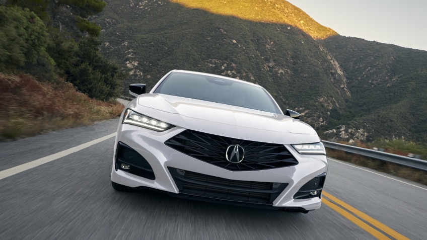 Front closeup of white TLX driving toward camera on highway in the mountains.