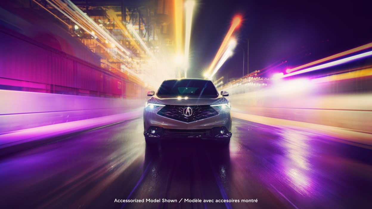 Front view of an Acura ADX on a city street with dramatic blurred light effects in the background