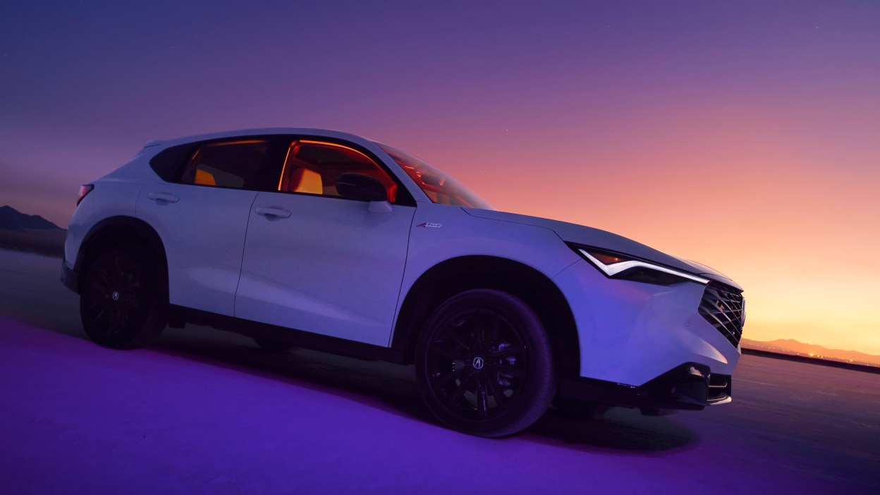 Side view of a white Acura ADX with a sunset in the distance.