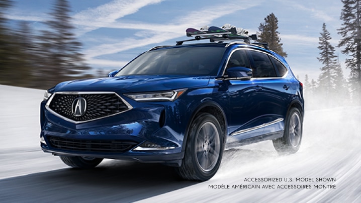 A blue MDX with a snowboard rack driving down a snowy road.