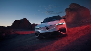 Front view of white ZDX parked in the desert at dusk with its headlights on, showered in red light.