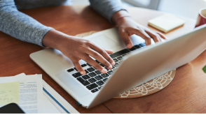 Gros plan en plongée des mains d’une femme tapant au clavier de son ordinateur portable sur une table en bois.
