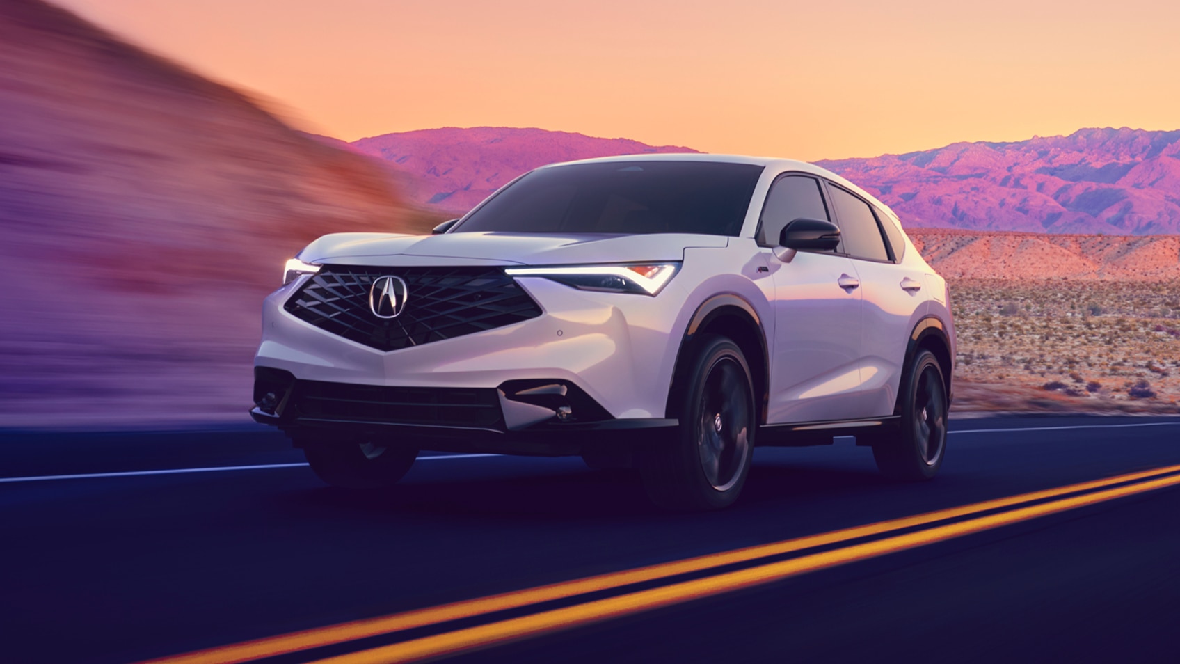 Acura ADX gris vu de face sur une route avec des montagnes colorées de violet en arrière-plan.