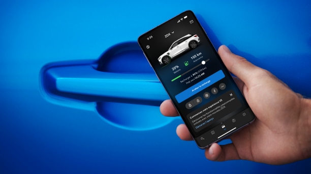 Gros plan d'une main tenant un téléphone intelligent, sur une page d'application Acura EV, devant la poignée de porte d'un Acura ZDX bleu.